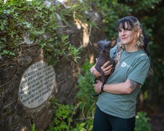 Helen Bruce, storyteller, holds a dog while standing next to a well.